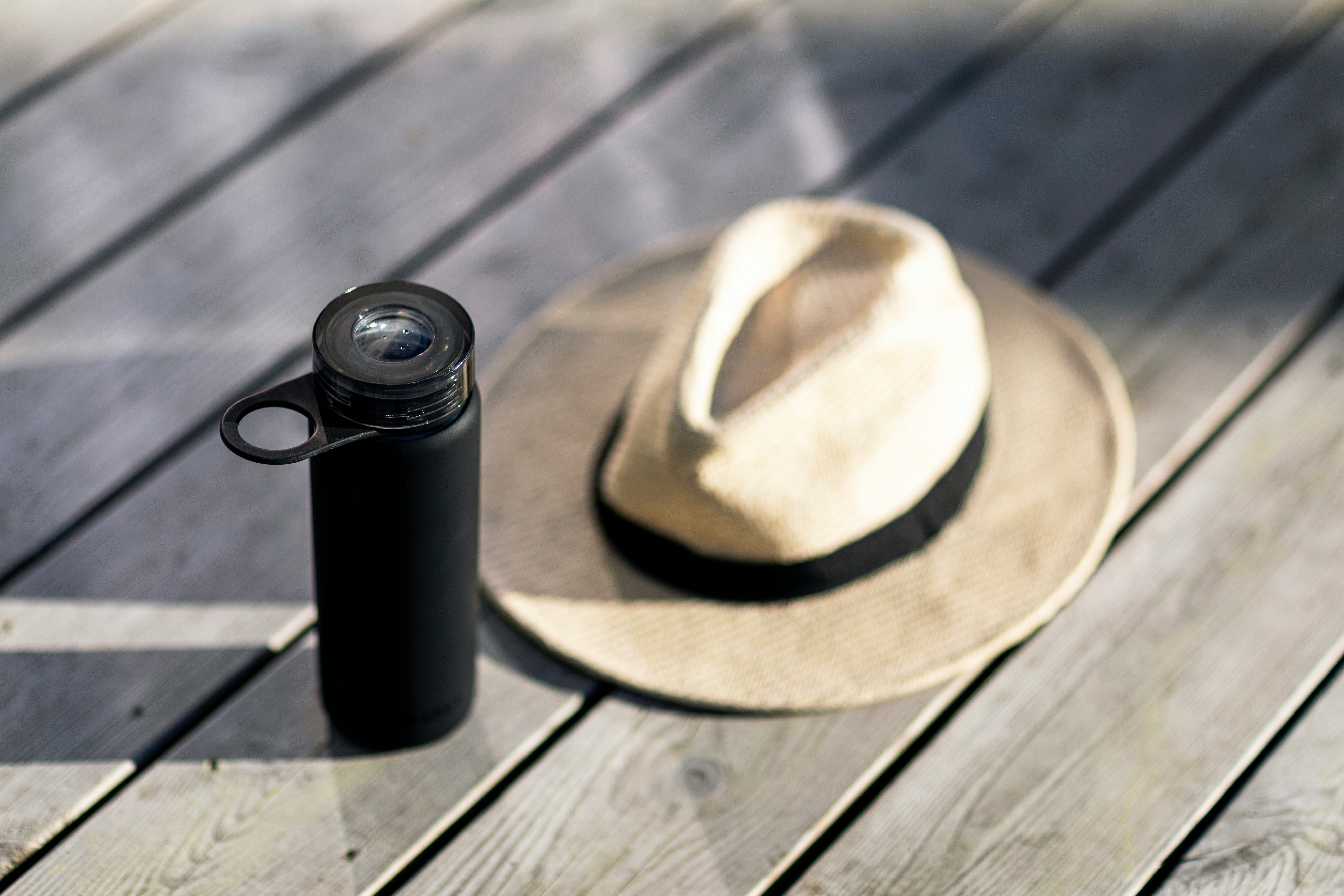 black and brown fedora hat beside black and silver tumbler on brown wooden table