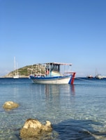 An inshore boat anchored near a rocky shoreline under a clear blue sky.