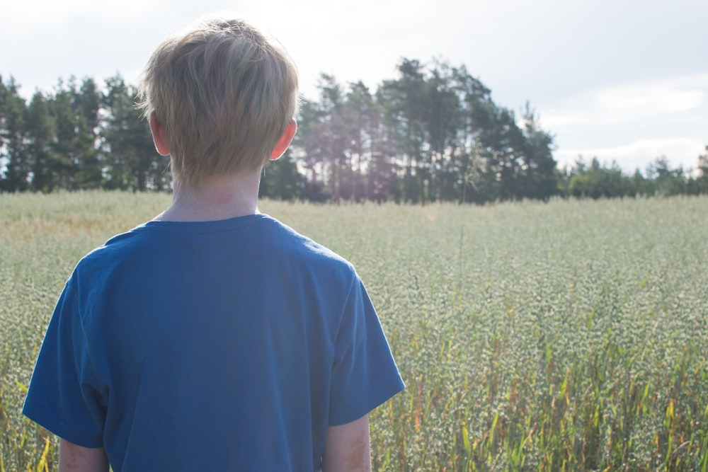 boy in blue crew neck t-shirt standing on green grass field during daytime