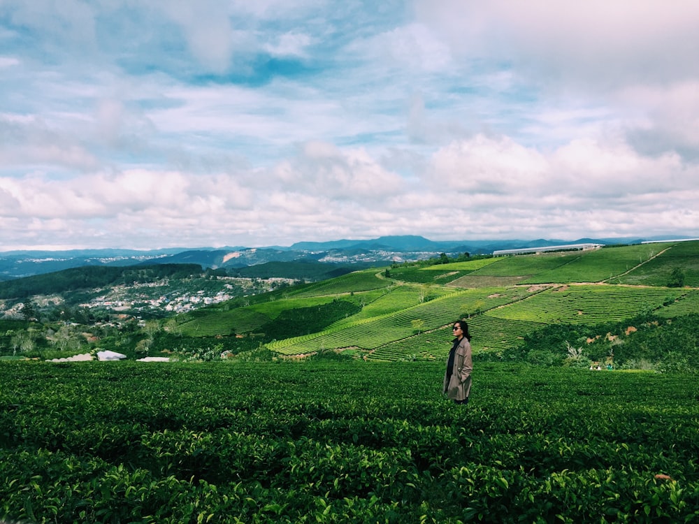 woman in white dress standing on green grass field under white clouds during daytime