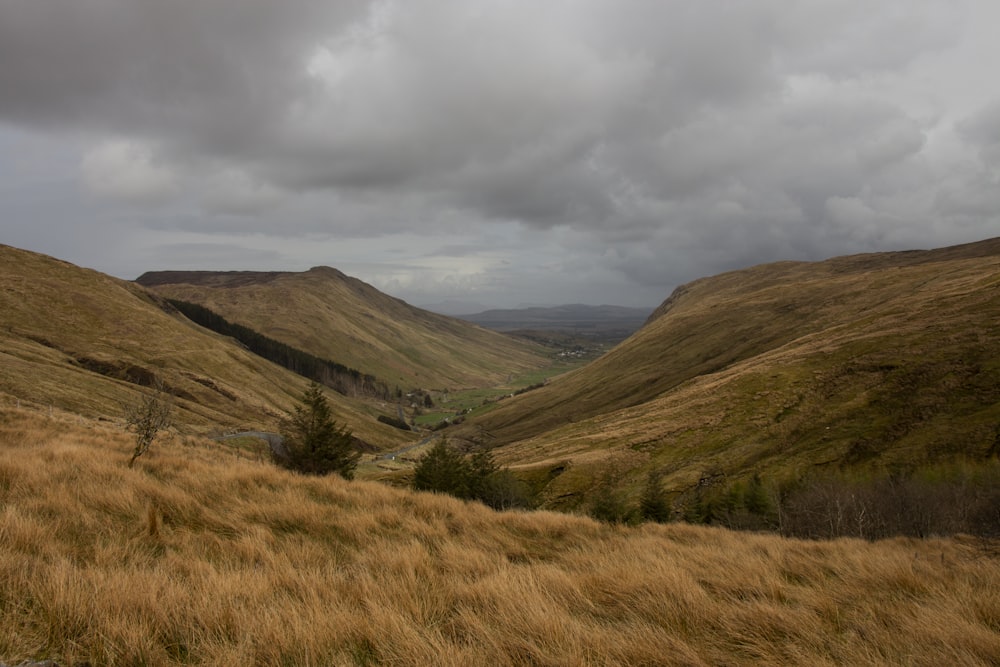 green grass field near mountain under cloudy sky during daytime