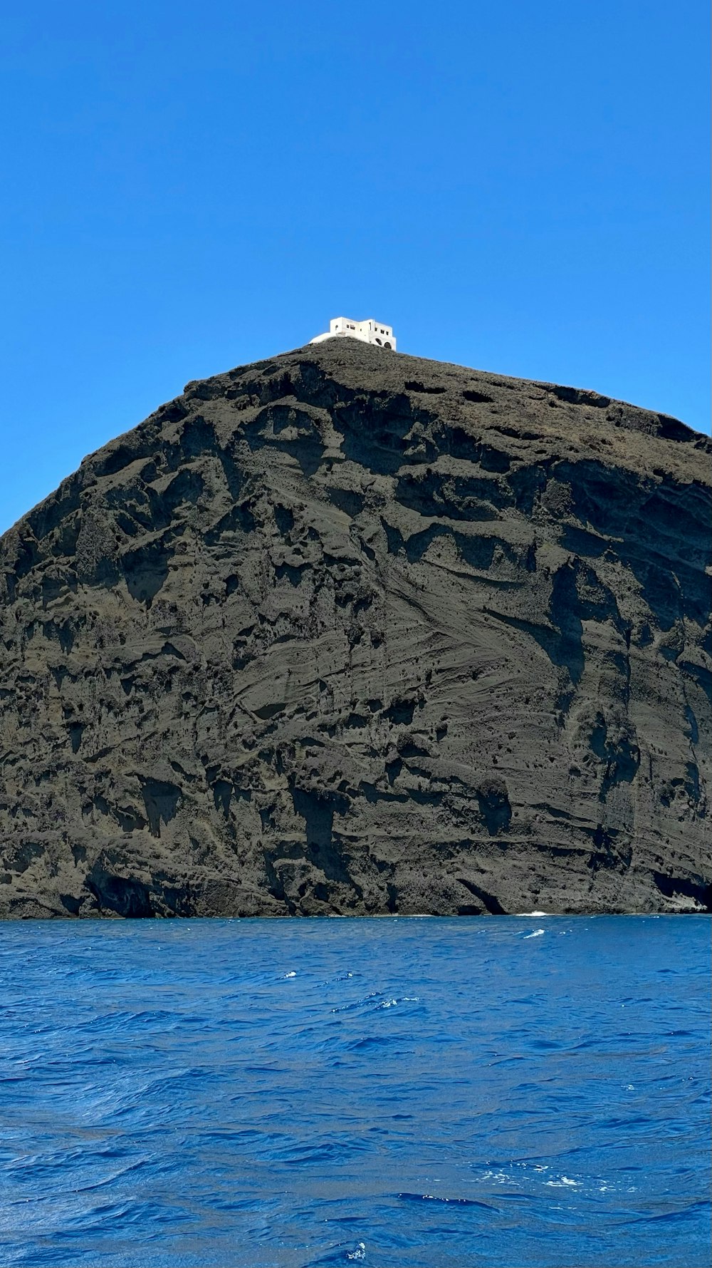 weißes und braunes Haus auf einer braunen Felsformation in der Nähe des blauen Meeres tagsüber