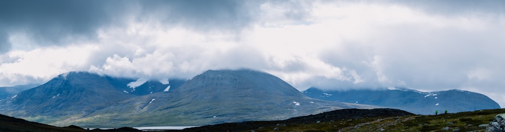 green grass field near mountain under white clouds during daytime