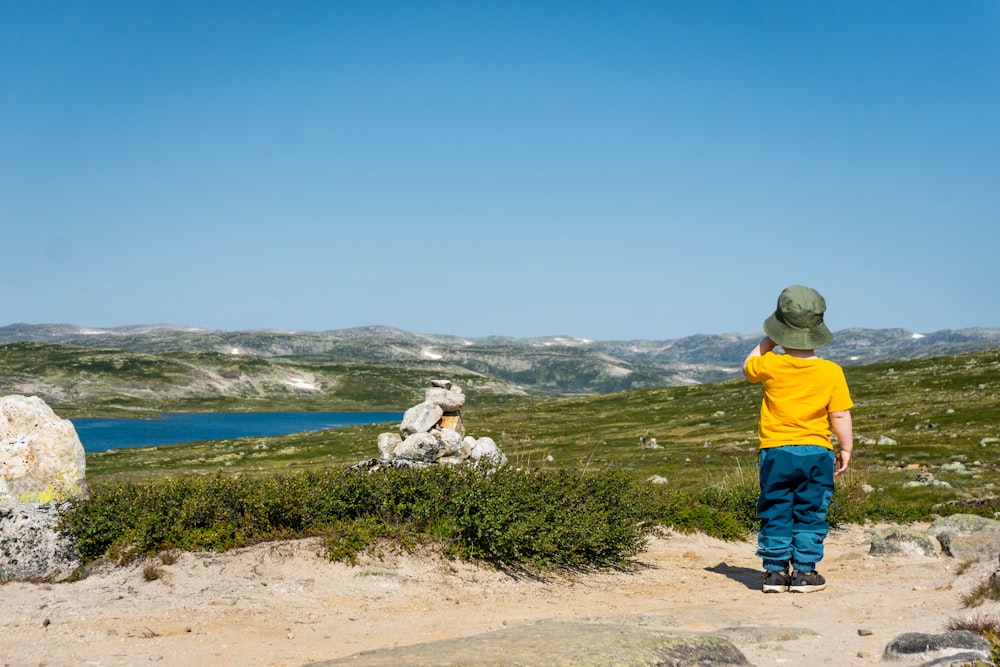 man in yellow hoodie standing on brown dirt near body of water during daytime