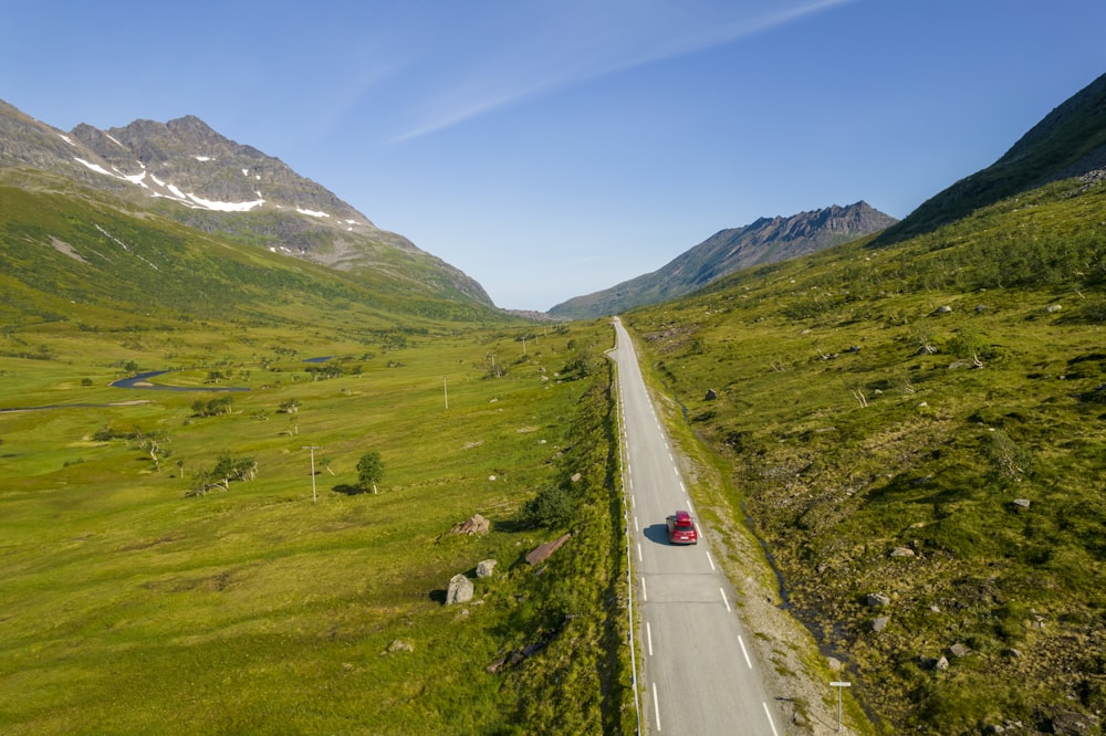 gray concrete road between green grass field near mountain under blue sky during daytime