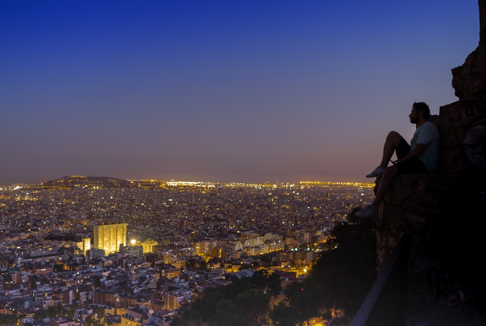 woman in black dress sitting on the edge of a building looking at the city during