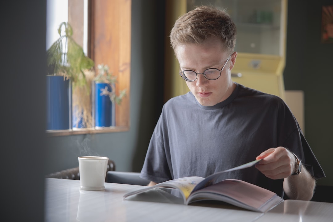 boy in blue crew neck shirt wearing eyeglasses reading book