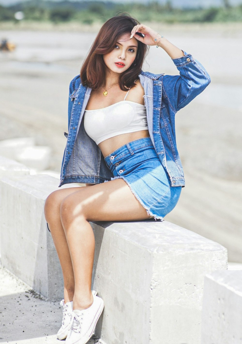 woman in blue denim jacket and white crop top and blue denim shorts sitting on concrete