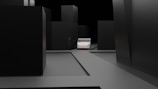 A minimalist, dark urban scene with tall, featureless black buildings surrounding a central, small, white vehicle. The ground is flat and gray, contributing to the stark, almost abstract feel of the environment.