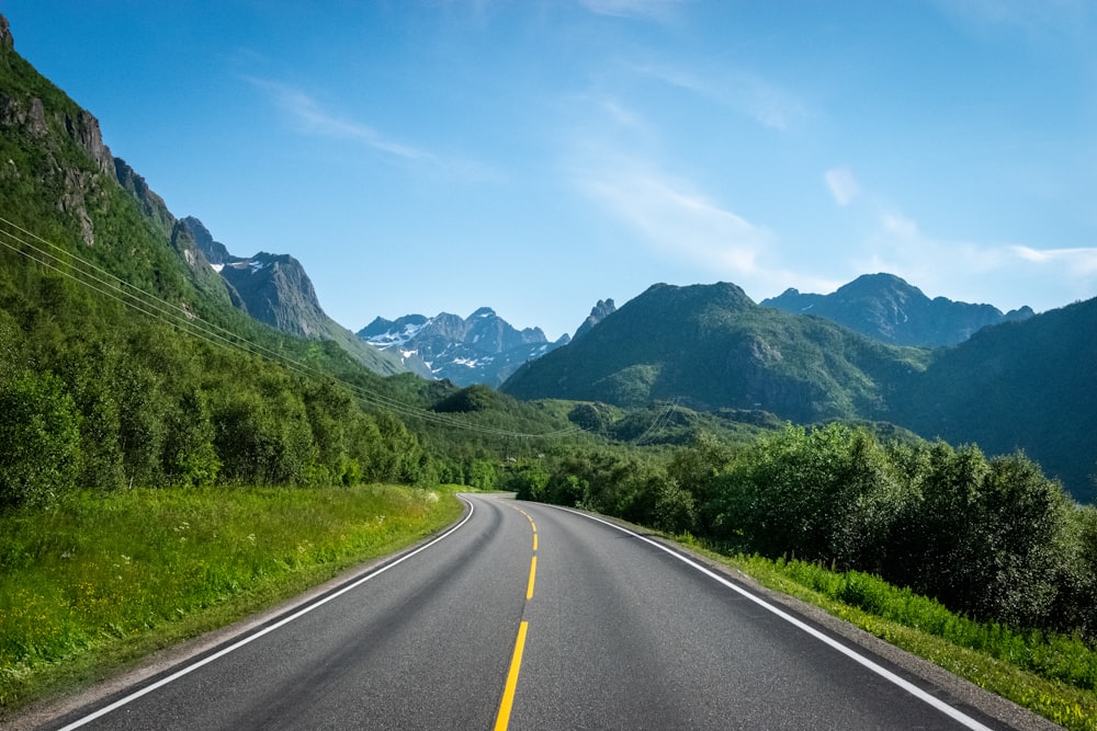 gray concrete road near green grass field and mountains during daytime