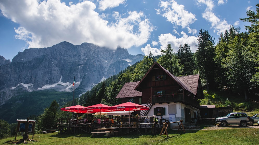 brown wooden house near green trees and mountain under white clouds during daytime