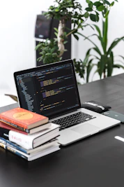 A young student happily working on a laptop surrounded by coding books and notes