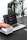 A workspace featuring a laptop displaying code, accompanied by a stack of books. The background includes green plants, creating a fresh and vibrant atmosphere. The desk also has a smartphone and a closed notebook.