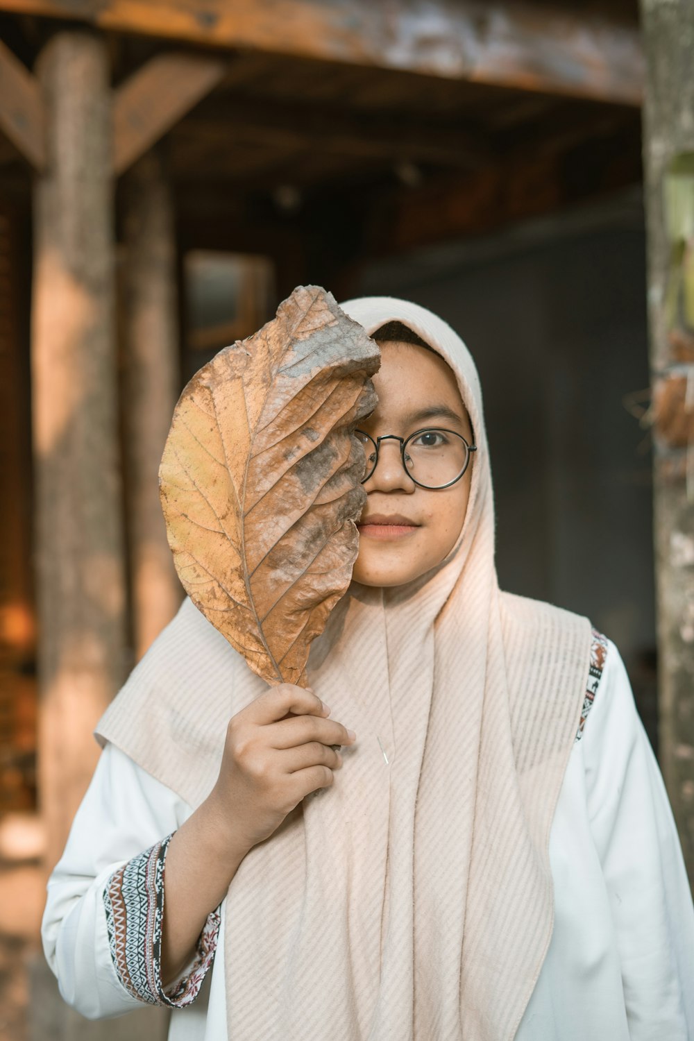 woman in white hijab covering her face with brown leaf