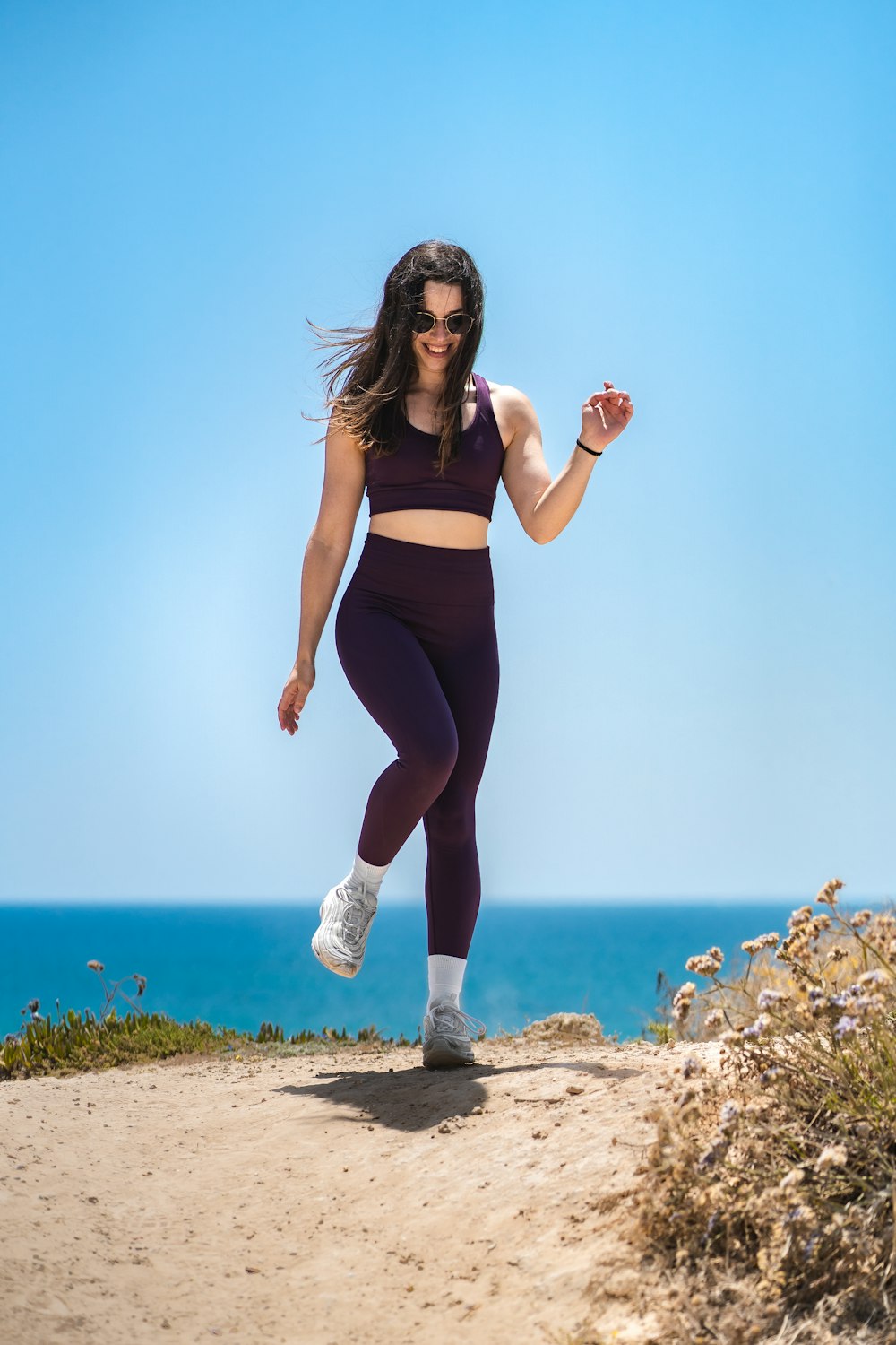woman in black sports bra and black leggings standing on rock near sea during daytime