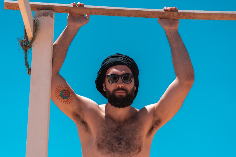 topless man wearing black sunglasses holding on blue metal bar