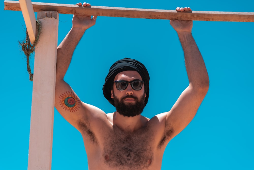 Hombre en topless con gafas de sol negras sosteniendo una barra de metal azul
