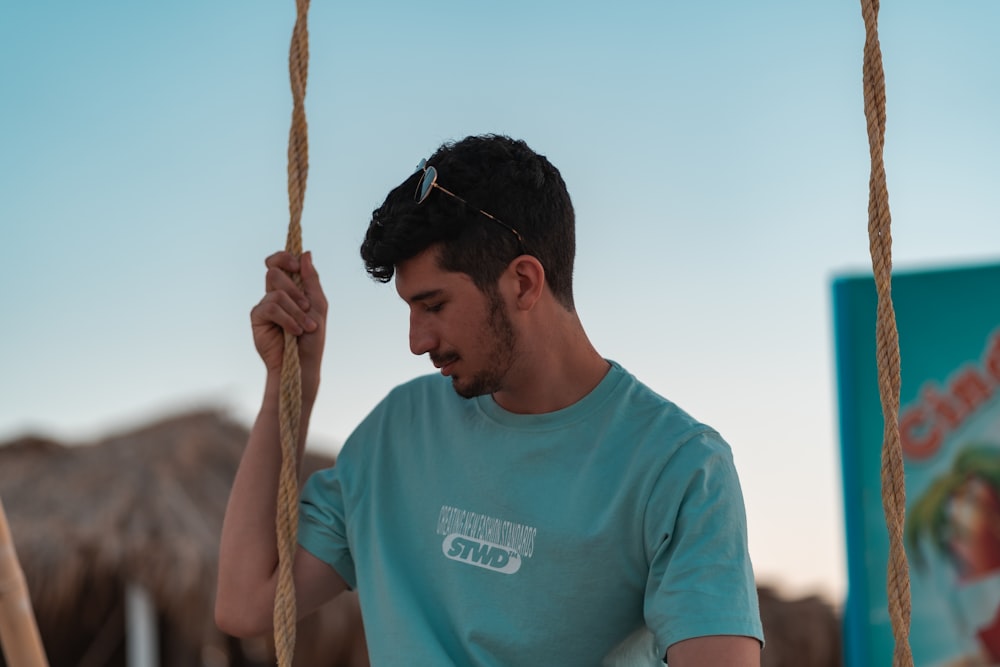 man in blue crew neck t-shirt holding brown rope during daytime