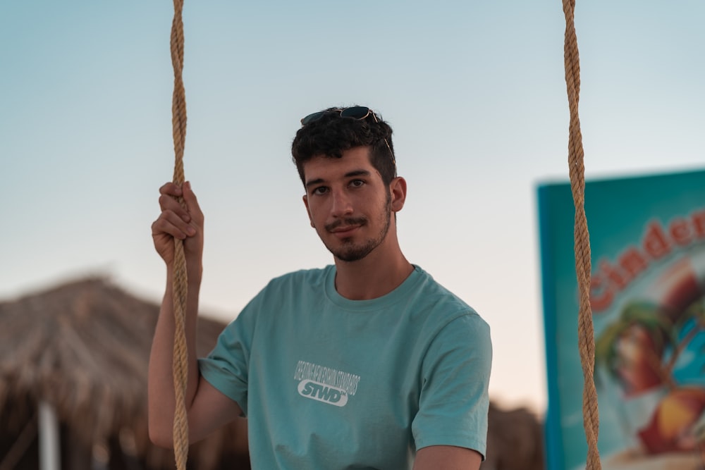 man in teal crew neck t-shirt holding brown rope
