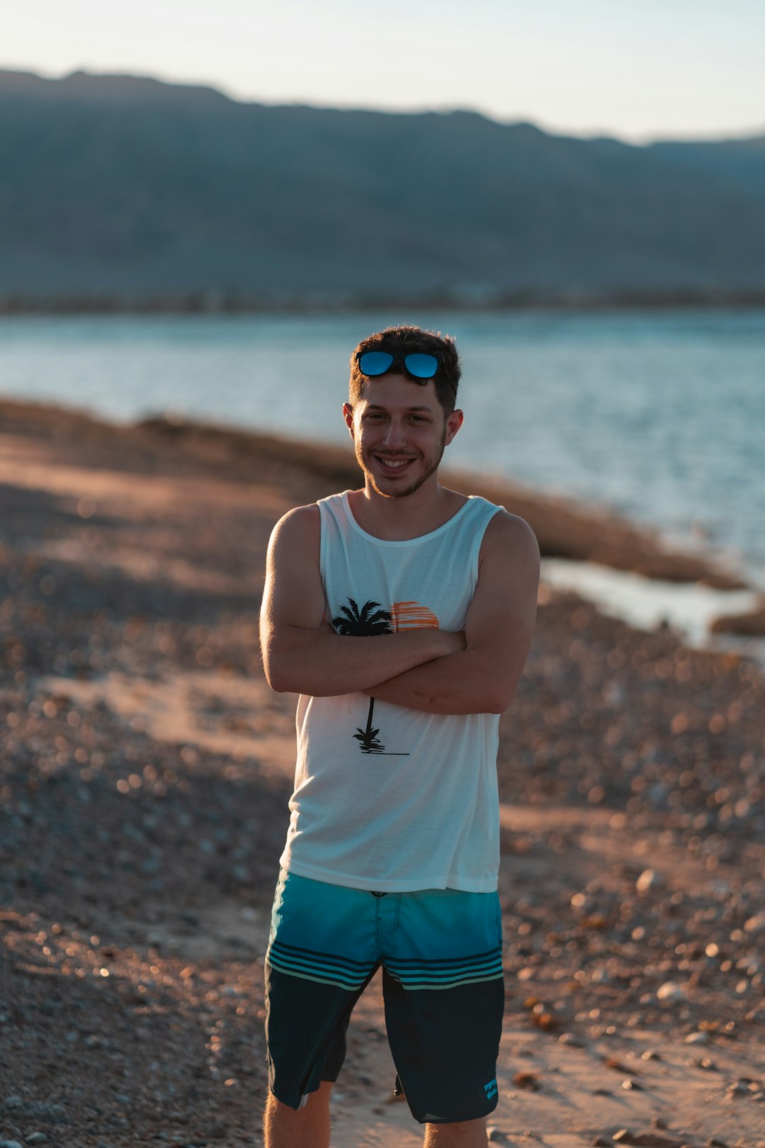 man in white tank top and blue shorts standing on shore during daytime