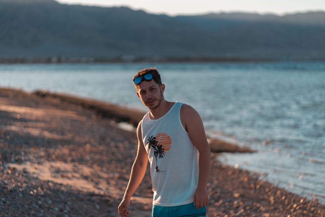 man in white tank top and blue shorts standing on shore during daytime