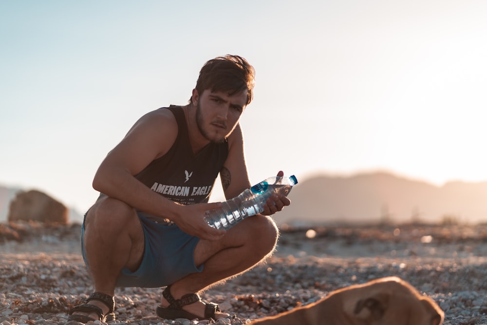 man in black tank top and blue denim shorts sitting on brown sand during daytime