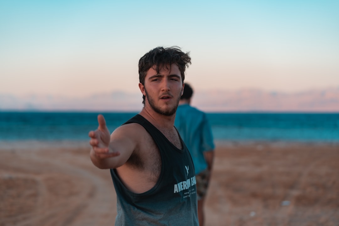 man in black and blue tank top standing on brown sand during daytime