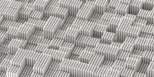 A pattern of densely packed, vertically aligned cylindrical shapes creating an abstract, geometric landscape. The arrangement forms a textured surface with varying heights, reminiscent of a futuristic cityscape or digital terrain.