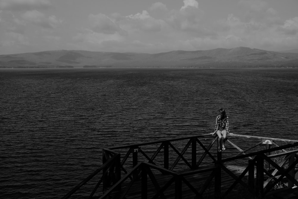 grayscale photo of woman walking on wooden dock