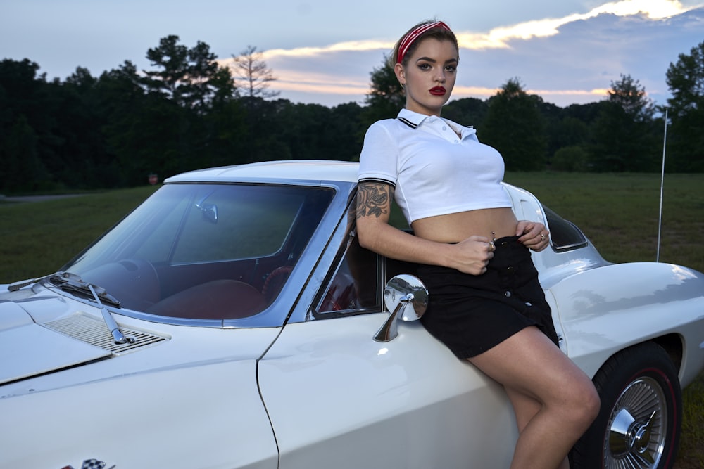 woman in white polo shirt and black skirt leaning on white car