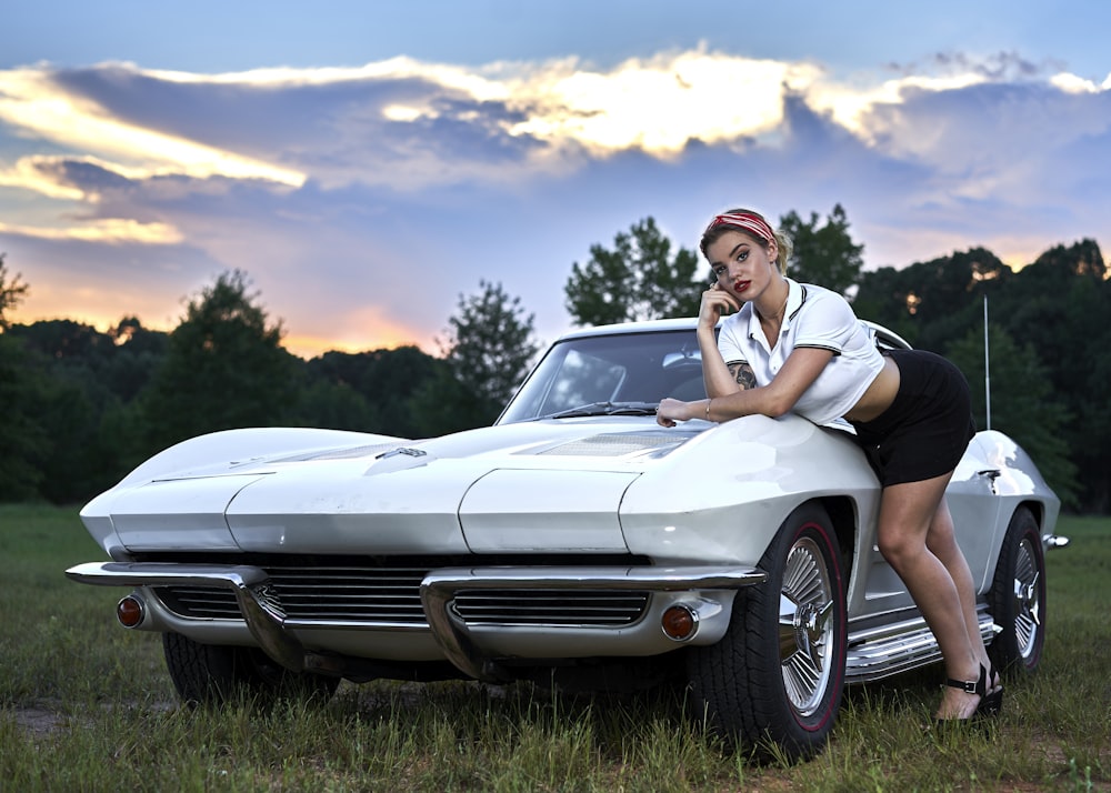 man in white t-shirt and black shorts sitting on white chevrolet camaro