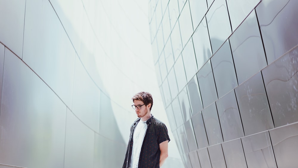 man in black t-shirt standing beside white wall