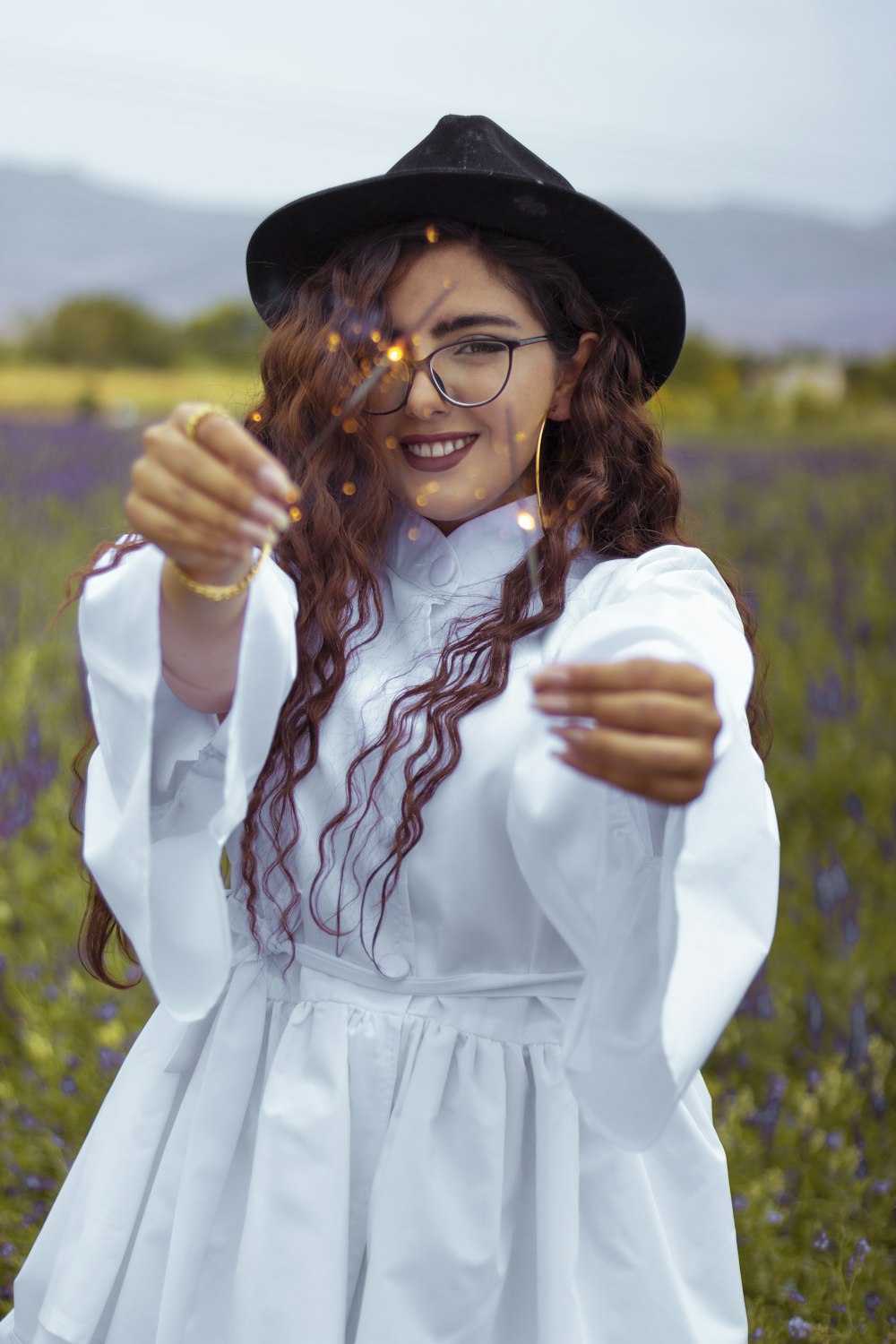 lächelnde Frau im weißen langärmeligen Kleid mit schwarzem Hut