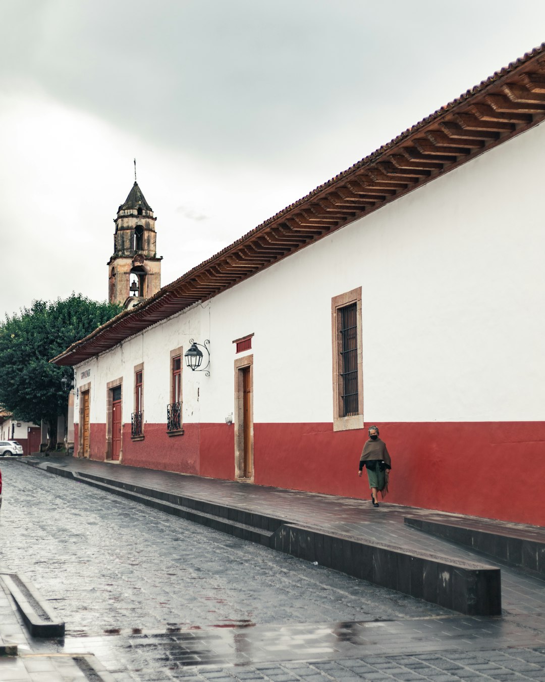 woman in green jacket walking on sidewalk near white and red concrete building during daytime