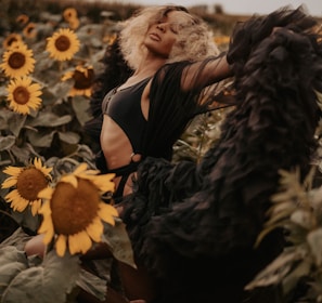 woman in black dress sitting on white flower field during daytime