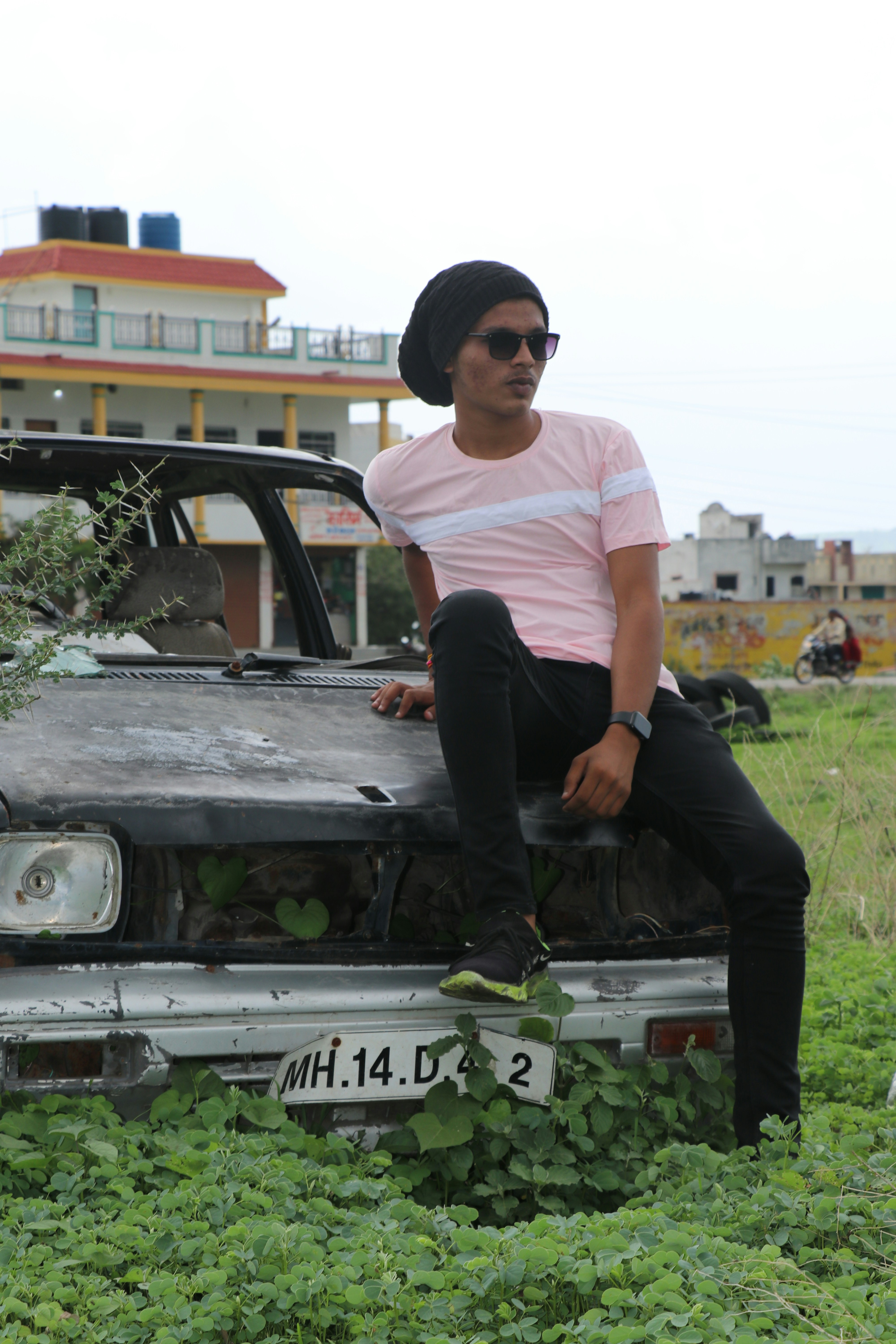 man in white crew neck t-shirt and black pants sitting on green car during daytime