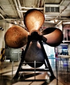 Stacks of ship propellers lined up in a warehouse under bright lights.