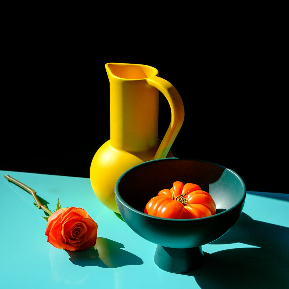 orange and red roses in white ceramic bowl beside yellow pitcher