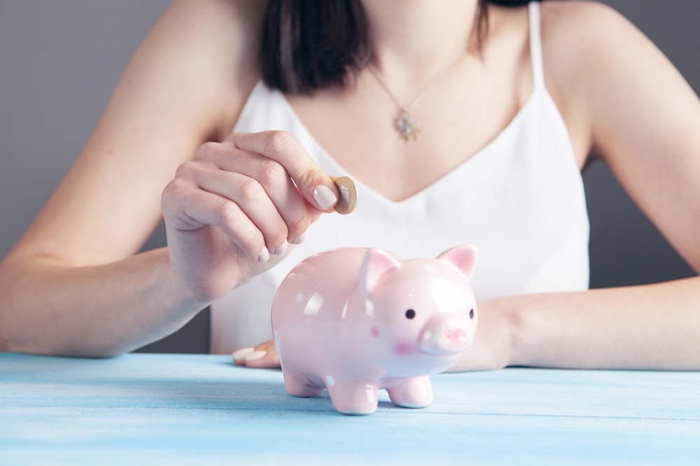 woman in white tank top holding pink pig figurine