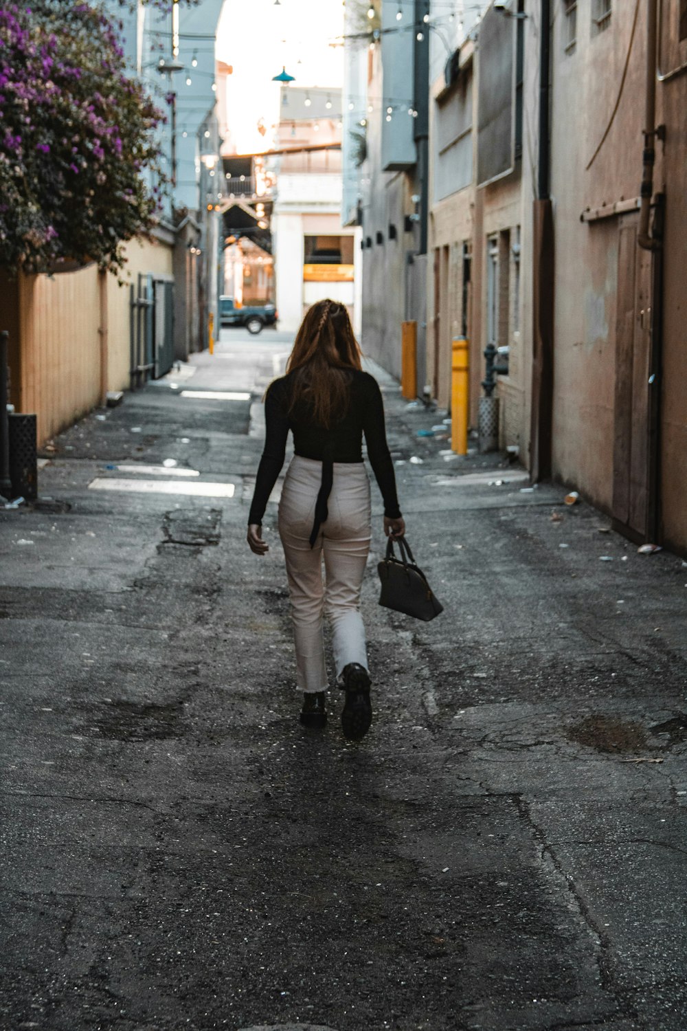 woman in black jacket and white pants walking on sidewalk during daytime