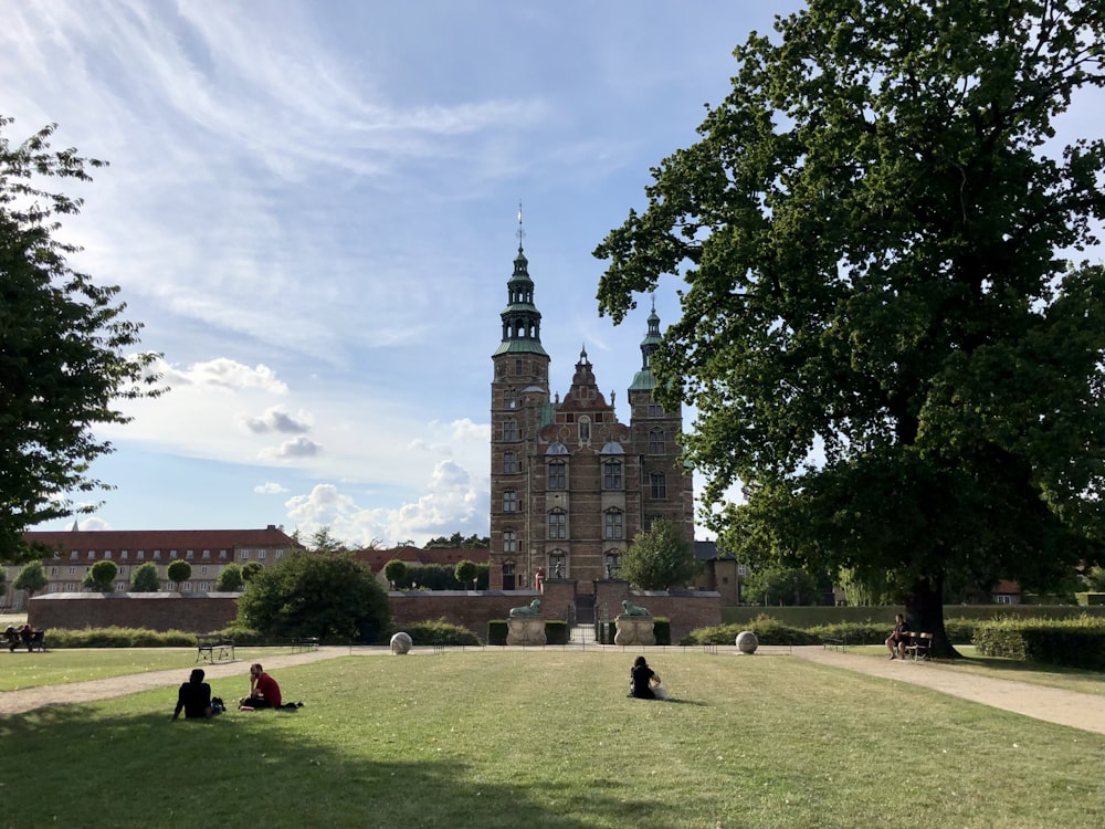 people sitting on green grass field near brown concrete building during daytime