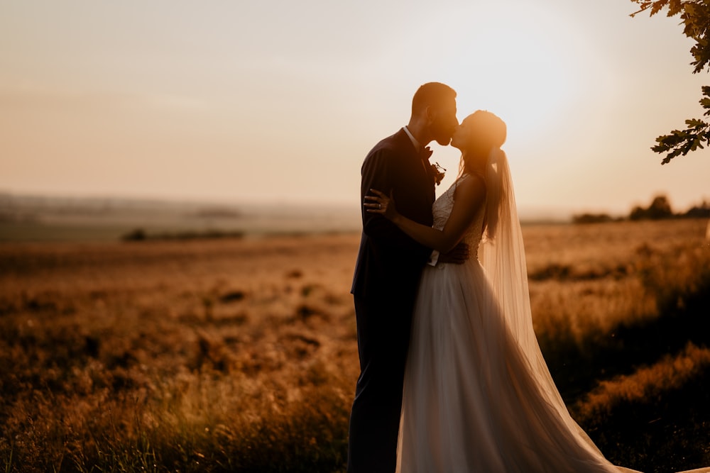 man and woman kissing on brown grass field during sunset