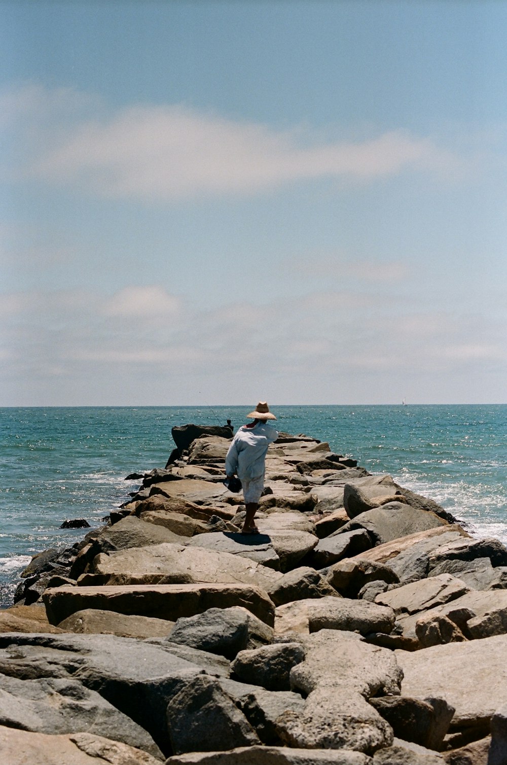 man in gray jacket sitting on gray rock near sea during daytime