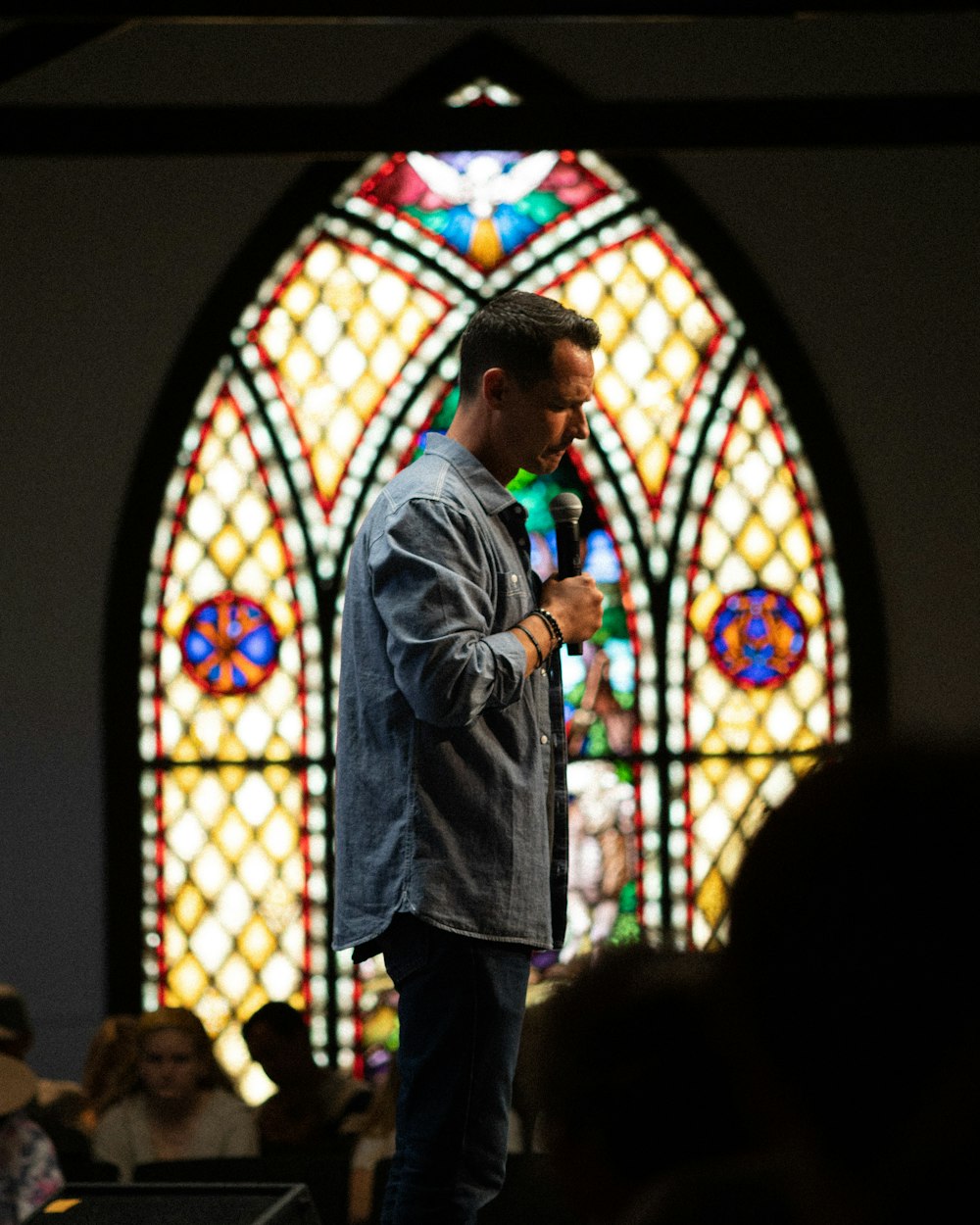 man in gray coat standing in front of blue and white stained glass
