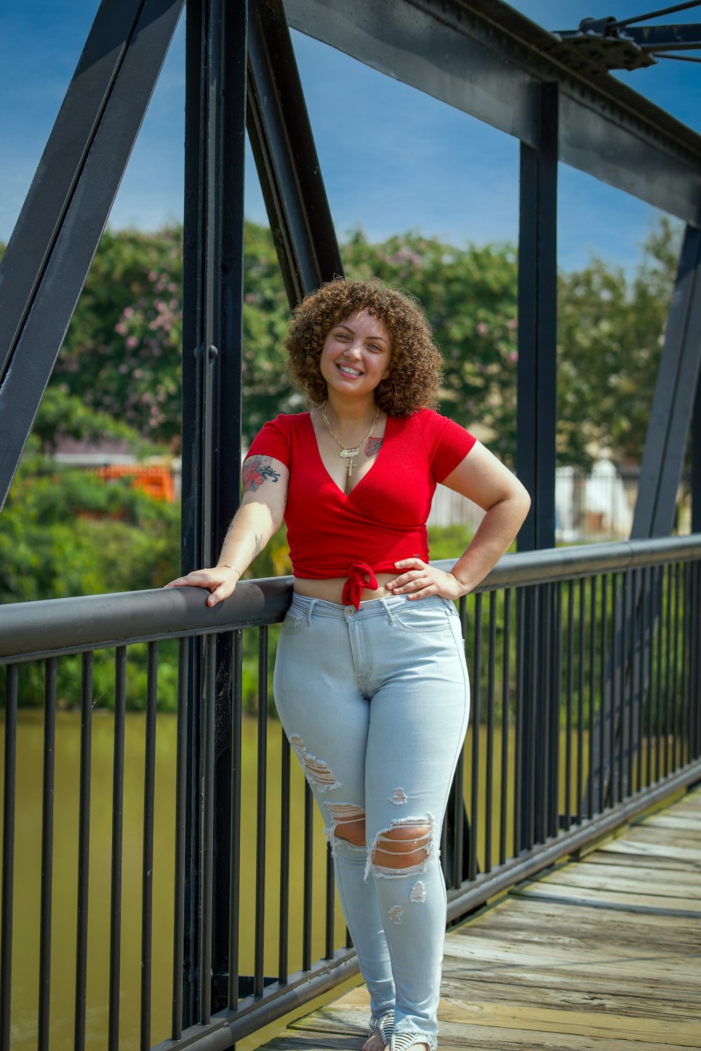 woman in red tank top and white denim jeans standing on black metal railings during daytime