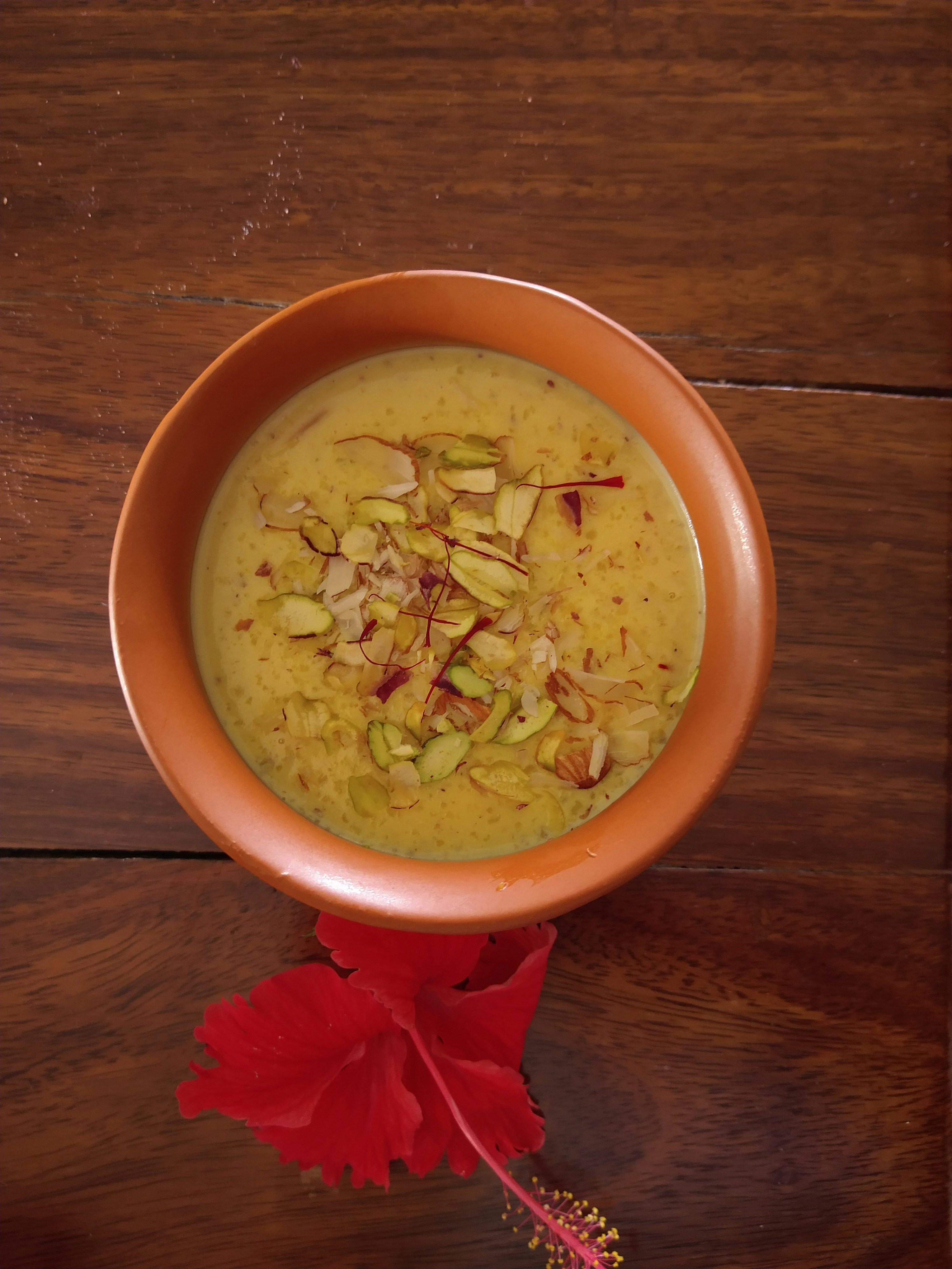 Creamy white kheer dessert in a clay bowl garnished with saffron and nuts, bright warm kitchen lighting