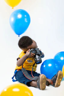 A cheerful child holding a video camera against a bright solid color background.