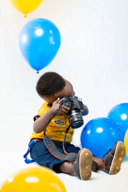 A cheerful child holding a video camera against a bright solid color background.