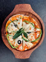 A hot, cheesy pizza topped with fresh tomatoes, olives, and basil leaves on a rustic wooden board.