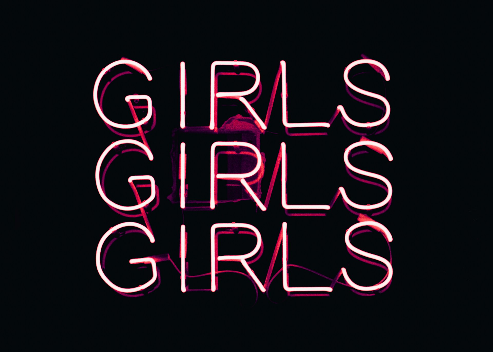 Neon pink lettering spells out the word 'GIRLS' three times in bold, stacked columns against a dark background.
